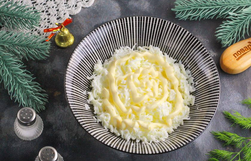 1. Этап. Крабовый салат на Новый год 2025: Отложенные белки натрите на терке с мелкими ячейками, посолите и заправьте 1 ст.л. майонеза.