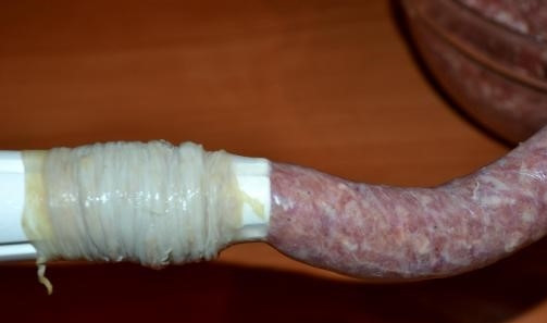 1. Этап. Колбаски из говядины: 5. Наденьте тщательно помытую кишку на приспособление для колбасы. Перед этим смажьте его постным маслом. Возьмите немного фарша, заложите его в мясорубку. Не спеша набивайте оболочку. Как можно чаще формируйте «звенья» колбаски.