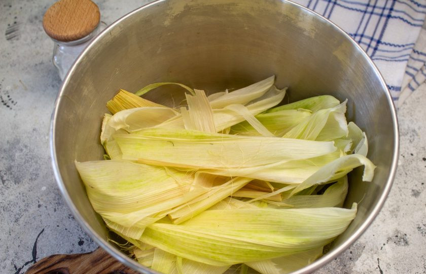 1. Этап. Кукуруза в початках: Очистите кукурузу, при этом волоски‑рыльца выбросите, а листья оставьте — они ещё пригодятся. Листья выложите в большую, глубокую кастрюлю. Не игнорируйте этот процесс — с листьями, вкус у кукурузы получается более насыщенный и ароматный.