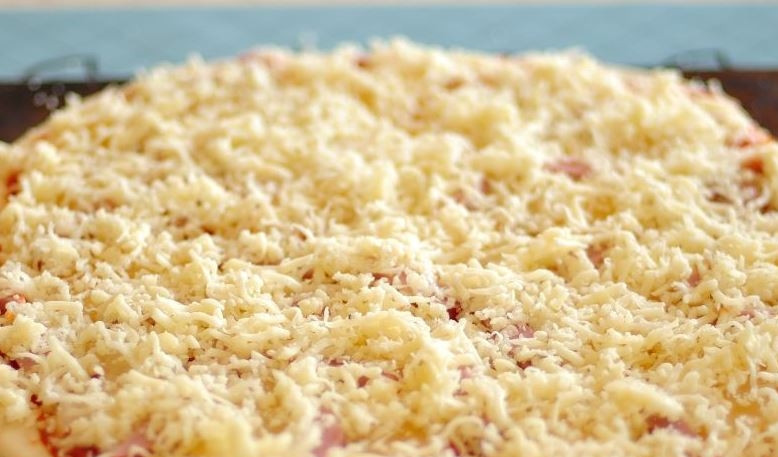 1. Этап. Домашняя пицца в духовке: Натрите на терке любой сорт твердого сыра. Лучше выбирать те, которые хорошо плавятся. Натрите сыр на терке и присыпьте им пиццу.
