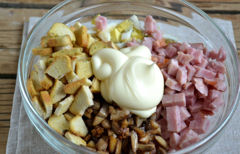 1. Этап. Салат с ветчиной и грибами: Смешайте ветчину и яйца с обжаренными грибами и сухариками. Заправьте все майонезом.