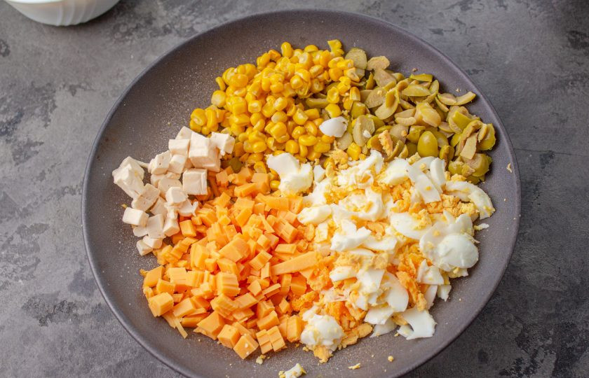 1. Этап. Салат Початок кукурузы: Куриные яйца отварите вкрутую, остудите и очистите. Яйца, оба вида сыра и оливки нарежьте мелко, добавьте 2 столовые ложки кукурузы от общей нормы. Также, по желанию, сыр и яйца можно натереть на терке.