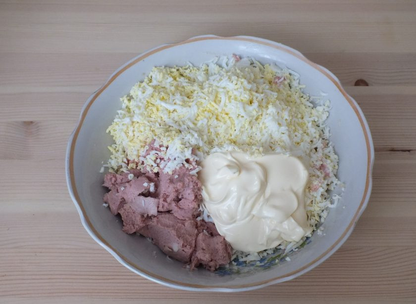 1. Этап. Закуска пикантная на Новый год Крысы: В чашу натрите на мелкой терке плавленый сыр, яйца. Добавьте измельченный чеснок, печеночный паштет и майонез.