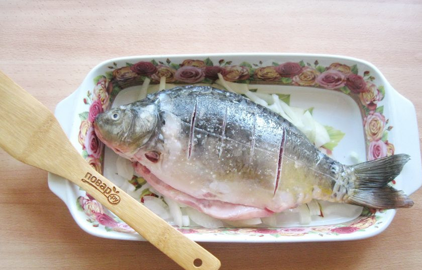 1. Этап. Карп в духовке на луковой подушке: На рыбе сделайте надрезы и посолите внутри и снаружи. Выложите на луковую подушку в форму.