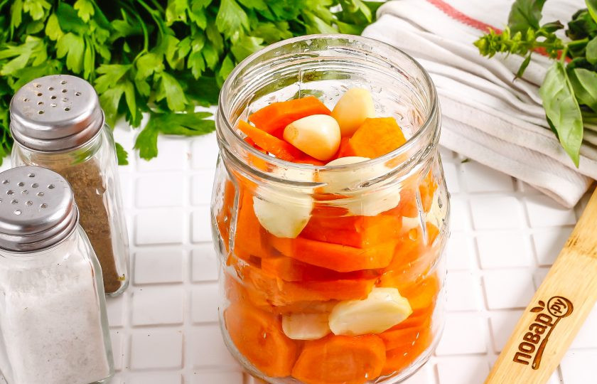 1. Этап. Маринованный чеснок с морковью на зиму: Морковь нарежьте шайбочками и выложите в банку вместе с чесночными зубчиками.