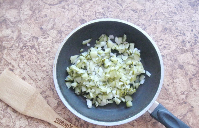 1. Этап. Солянка как в ресторане: Репчатый лук и соленый огурец мелко нарежьте и выложите в сковороду с подсолнечным маслом.