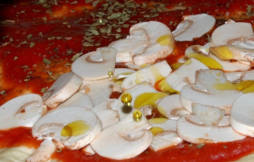 1. Этап. Сырная пицца Четыре сезона: 5. Условно разделите круглую основу на 4 части, выложите на одну сторону грибы, добавьте несколько капель оливкового масла.