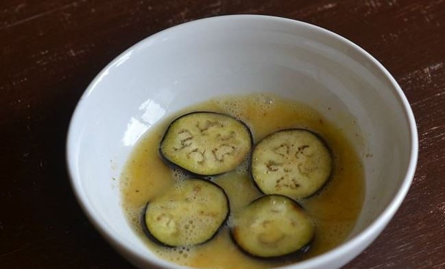 1. Этап. Баклажаны, запеченные с чесноком: Измельчите чеснок при помощи пресса или натрите на мелкой терке. Добавьте его к яйцу. Выложите в мисочку кружочки баклажанов и хорошенько их смочите.