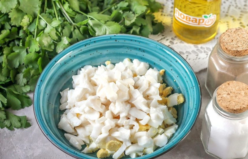 1. Этап. Салат с кальмарами и кинзой: Слейте маринад с консервированных кальмаров и нарежьте их такими же кубиками, как и отварные яйца. Добавьте в емкость.