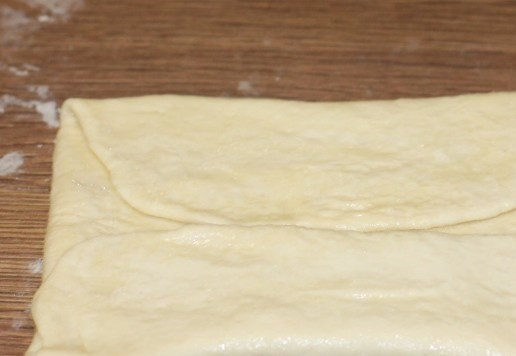 1. Этап. Слоеные пирожки с луком и картошкой: 9. Складываем край пласта до середины и смазываем маслом.
