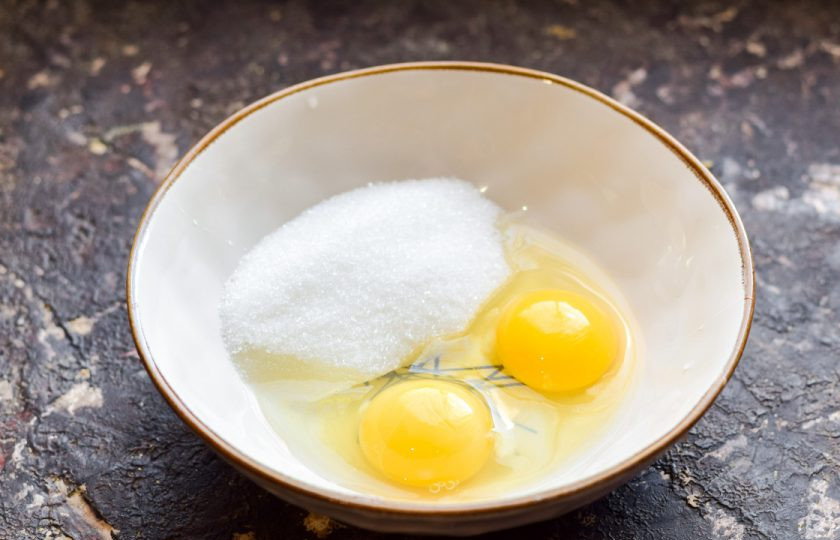 1. Этап. Шоколадные оладьи на молоке: Вбейте в миску куриные яйца и добавьте сахар.