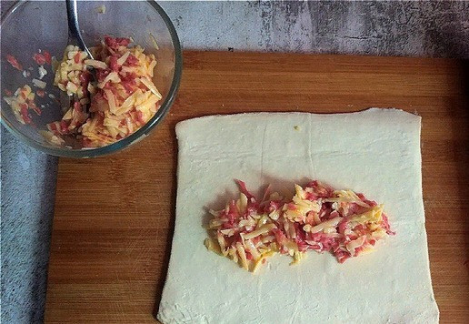 1. Этап. Слойки с колбасками и сыром: 250 г теста делим пополам и немного раскатываем. Выкладываем начинку (см. фото).