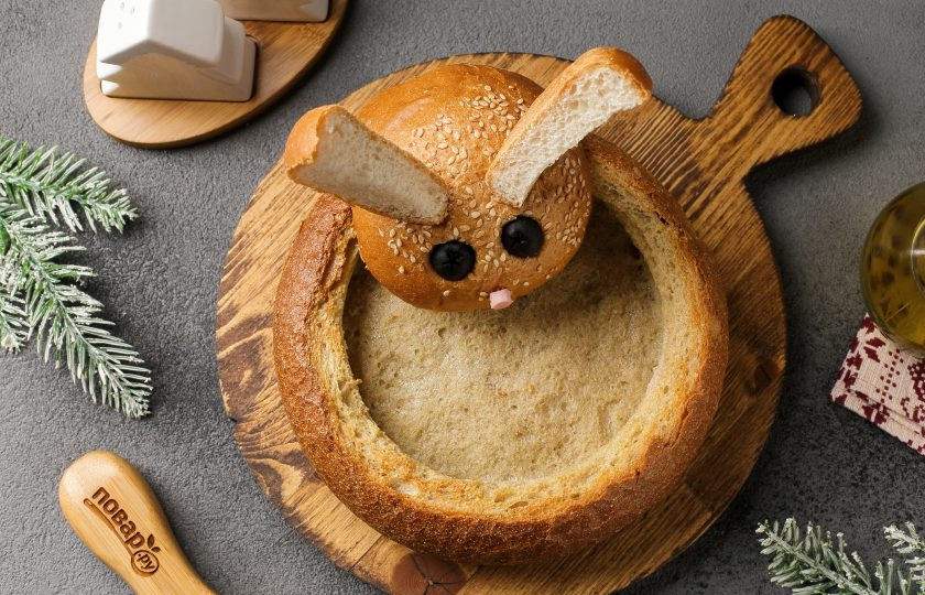 1. Этап. Сырный крем-суп с грибами в хлебе Веселый Кролик: Проткните хлеб в двух местах зубочистками и прикрепите на них голову кролика, как на фото. Налейте крем-суп в подготовленную хлебную тарелку, украсьте по вкусу и подавайте к столу.