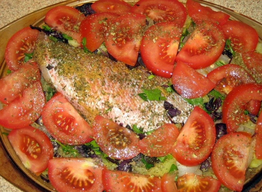 1. Этап. Морской окунь запеченный: Вокруг окуня равномерно выкладываем дольки помидоров (как на фото). Затем аккуратно и равномерно, не пропуская ни одного сантиметра, полить блюдо оливковым маслом. Влить в форму для выпекания 100 мл. воды. И отправляем наше блюдо в предварительно разогретую до 220 градусов духовку на 45 минут.
