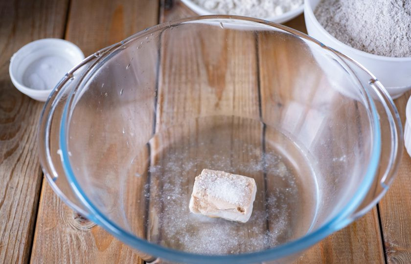 1. Этап. Булочки ржано-пшеничные: В просторную миску залейте теплую воду, добавьте дрожжи, сахар и соль. Перемешайте все венчиком до растворения дрожжей.