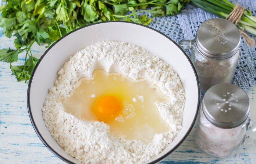 1. Этап. Тесто для пельменей по ГОСТу: Просейте пшеничную муку высшего сорта в глубокую миску или салатник. Рукой сделайте в муке углубление. Вбейте туда куриное яйцо и влейте воду: фильтрованную, холодную или теплую - на ваше усмотрение, но не газированную. Всыпьте соль.