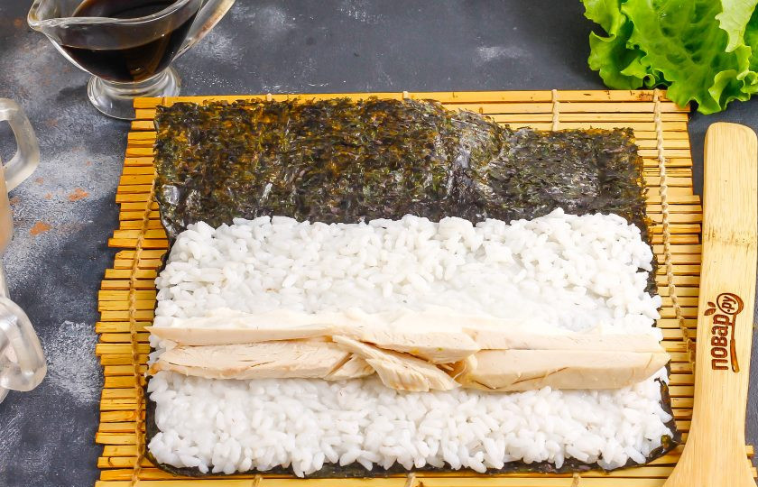 1. Этап. Роллы с курицей и ананасом: Выложите посередине слой сливочного сыра, на него — ломтики нарезанного отварного куриного филе.