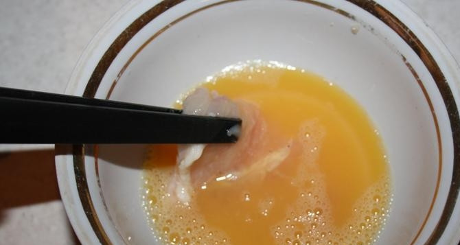 1. Этап. Мясо по-министерски: В пиалу вбейте сырое куриное яйцо, влейте к нему пятьдесят миллилитров воды и взбейте все вилкой или венчиком до однородности. Затем обмакните в яйцо кусочки курицы.