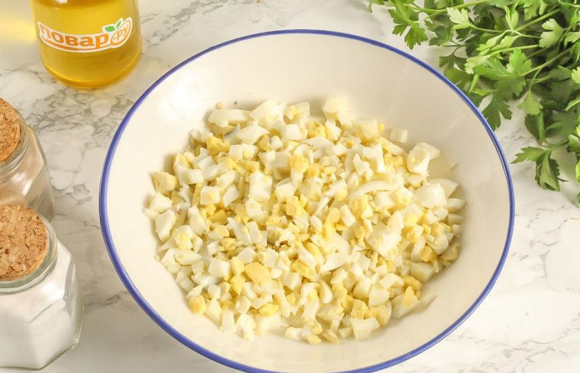 1. Этап. Салат с тунцом и кукурузой в тарталетках: Отварные куриные яйца очистите от скорлупы и промойте в воде. Затем нарежьте мелкими кубиками и выложите нарезку в салатник.