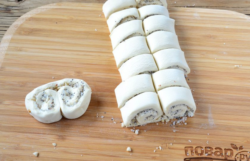 1. Этап. Ушки-завитушки: Порежьте рулетик на кусочки толщиной 2 см. Выложите заготовки на противень, застеленный пергаментом. Выкладывая каждую заготовку, слегка прижимайте ее к пергаменту.