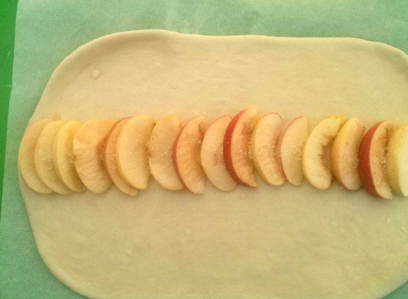 1. Этап. Сдобная плетенка с яблоками: Яблоко порежьте на тонкие ломтики. Выложите его красиво на середину прямоугольника, посыпьте сахаром.