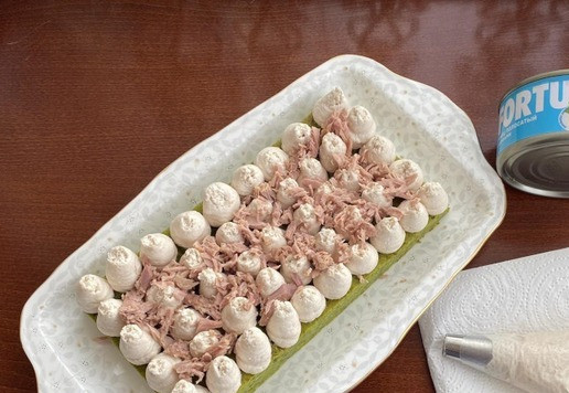 1. Этап. Закусочный шпинатный торт: Установите одну часть бисквита на сервировочное блюдо и отсадите крем по всей поверхности. Распределите половину нормы оставшегося тунца. Накройте сверху второй частью бисквита и повторите процесс. Верхний слой украсьте кремом и помидорами черри.