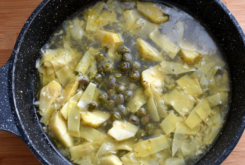 1. Этап. Куриная пикката с артишоком: Влейте вино и куриный бульон, выпарите их вполовину. Добавьте промытые каперсы и натертую свежую цедру. Чуть посолите и проварите пару минут.