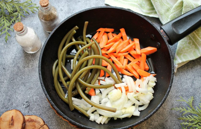 1. Этап. Папоротник со свининой: В сковороду налейте растительное масло, выложите морковь порезанную соломкой, резаный репчатый лук и папоротник, влейте воду. Поставьте в сковороду на средний огонь и тушите под крышкой 5-7 минут.