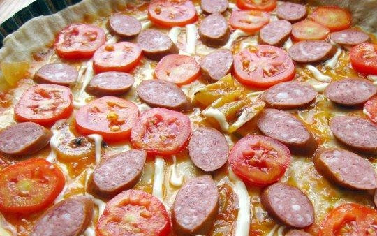 1. Этап. Пицца с копчёной колбаской: Нарежьте кружочками колбаску и помидоры. Распределите их по тесту.