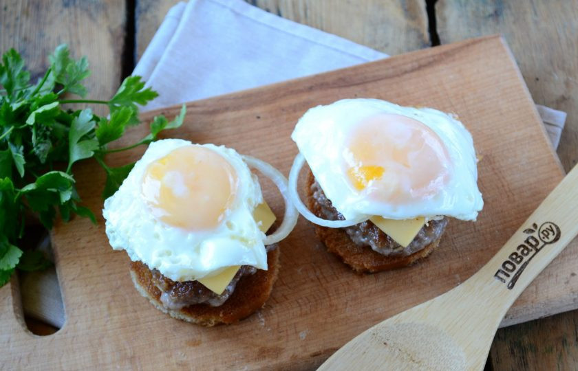1. Этап. Чизбургер с гренками и яйцом: Приготовьте яичницы любым удобным для вас способом. Как это делаю я: хорошо разогреваю сковороду, разбиваю яйца, немного солю, накрываю крышкой и уменьшаю огонь до минимума. Жарю несколько минут, пока белок на желтке слегка не побелеет. Очень важно оставить желток жидким. Готовое яйцо положите на чизбургер.