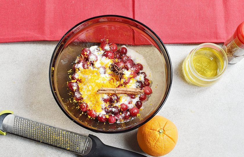 1. Этап. Клюквенный соус к мясу: Выложите клюкву в удобную миску для микроволновки. Засыпьте сахаром, добавьте мед. Положите пряности. Натрите цедру с апельсина, предварительно ошпарив плод кипятком.