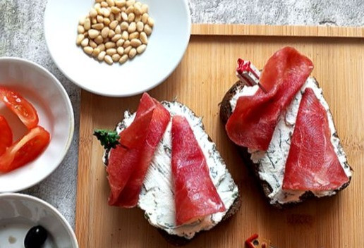 1. Этап. Закусочные брускетты: Хлеб щедро намазываем сыром с укропом. Немного сверху присолим и поперчим. Укладываем на него красиво по паре ломтиков сыровяленого филе. Я одно филе сверну 