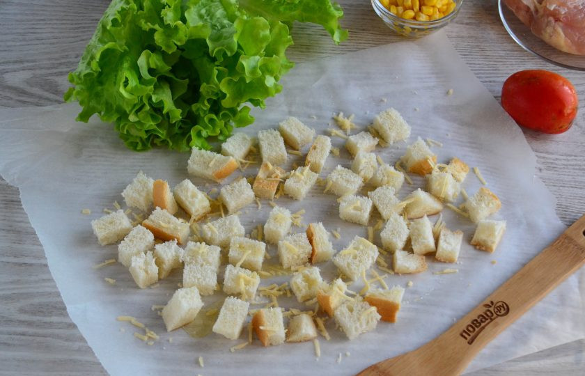 1. Этап. Салат с гренками: Выложите кубики хлеба на пергамент, сбрызните растительным маслом и присыпьте небольшим количеством натертого сыра. Отправьте в духовку, разогретую до 160 градусов и подсушите в течение минут 5-10. Время может варьироваться, зависимо от типа духовки и самого хлеба.