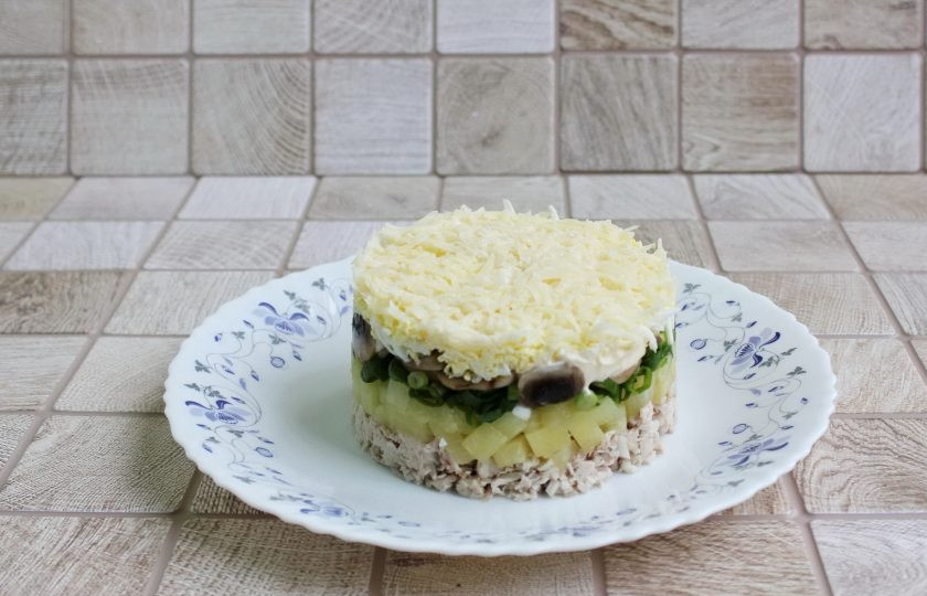1. Этап. Слоёный салат с ананасами, курицей и жареными грибами: Установите кулинарное кольцо на тарелку и собирайте салат слоями в следующем порядке. Первый слой курица, второй слой ананасы, третий зелёный лук и четвёртый грибы. После тёртые яйца и последний тёртый сыр.