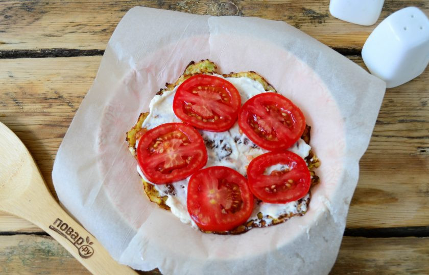 1. Этап. Кабачковый торт с помидорами и сыром: Начинайте собирать кабачковый торт. Тарелку застелите двумя полосками пергамента. Сверху положите первый кабачковый блин, смажьте его сырно-мойонезным 