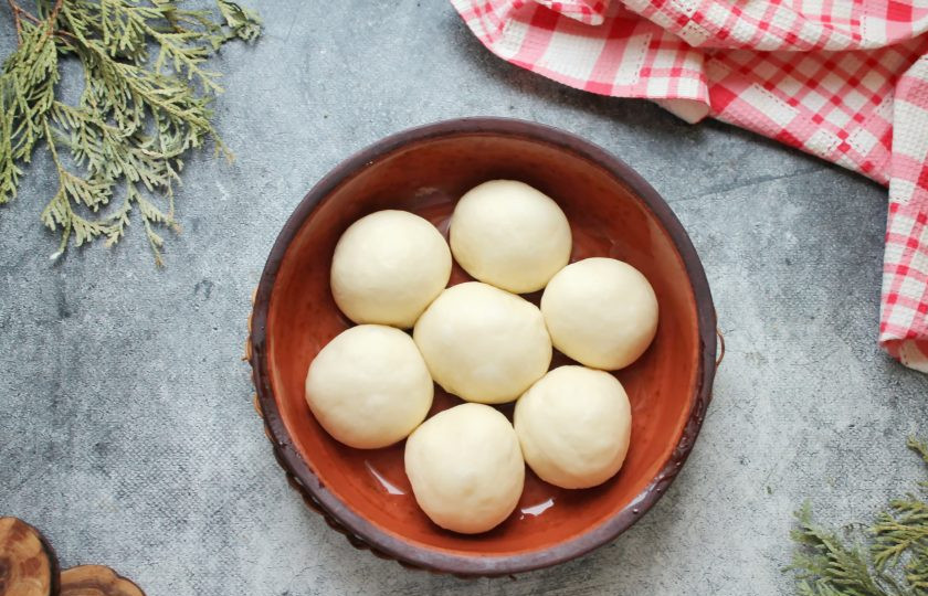 1. Этап. Чесночные булочки в духовке из дрожжевого теста: Форму для выпечки смажьте растительным маслом. Тесто разделите на части, скатайте шарики и выложите в форму на расстоянии. Форму покройте и оставьте на 10-15 минут для подъема.