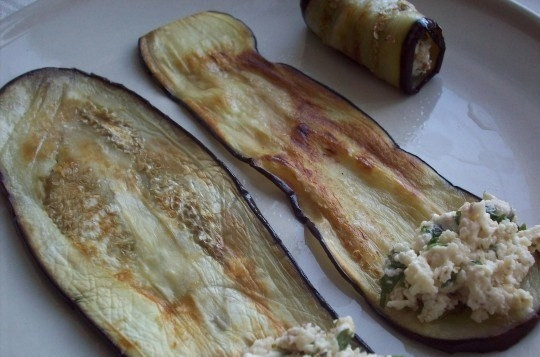 1. Этап. Рулетики из баклажанов с брынзой: Выкладывайте чайной ложкой начинку на край полоски баклажана и сворачивайте его трубочкой. Получившиеся рулетики поставьте в холодильник, чтоб они остыли. Подавайте к столу, украсив зеленью.