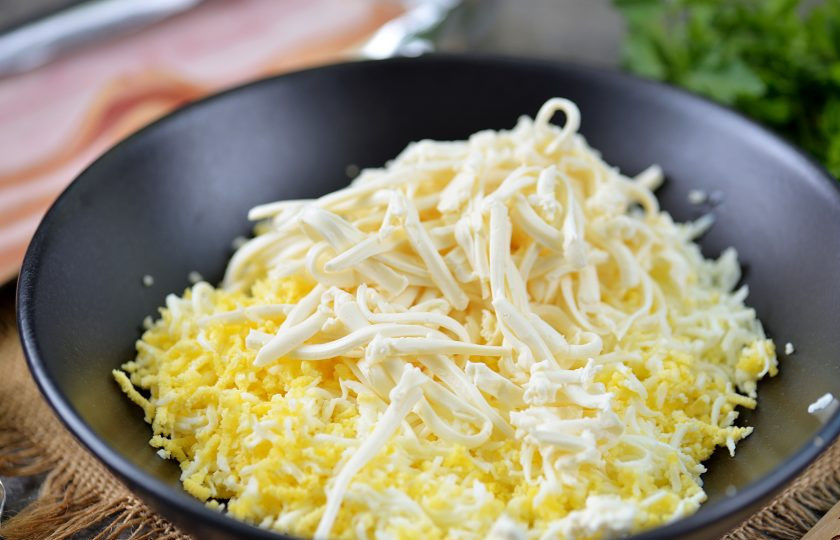 1. Этап. Рулетики из бекона с сыром и яйцом: Натрите яйца на мелкой терке, а плавленый сыр на крупной, переложите эти продукты в глубокую миску.