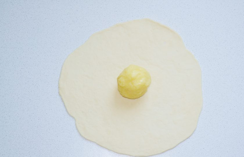1. Этап. Хычины на кефире: Отщипните кусочек теста и раскатайте на столе. Из начинки сформируйте шарик и выложите его в центр.