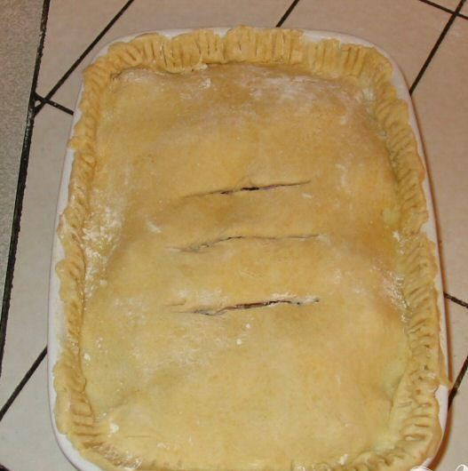 1. Этап. Пирог с курицей и беконом: 4. Через полчаса достать тесто из холодильника, удалить пищевую пленку и разровнять тесто руками. Тщательно посыпать рабочую поверхность мукой. Скалкой раскатать тесто по размеру Ваше формы, смазать края формы водой, чтобы тесто прилипло к ним. Положить тесто поверх курицы и залепить края. Сделать 3 больших надреза, чтобы выходил пар. Смазать тесто молоком.