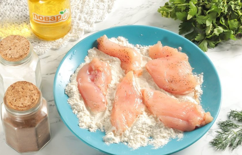1. Этап. Наггетсы на сковороде: Высыпьте пшеничную муку на тарелку и обваляйте ломтики куриного филе с обеих сторон.