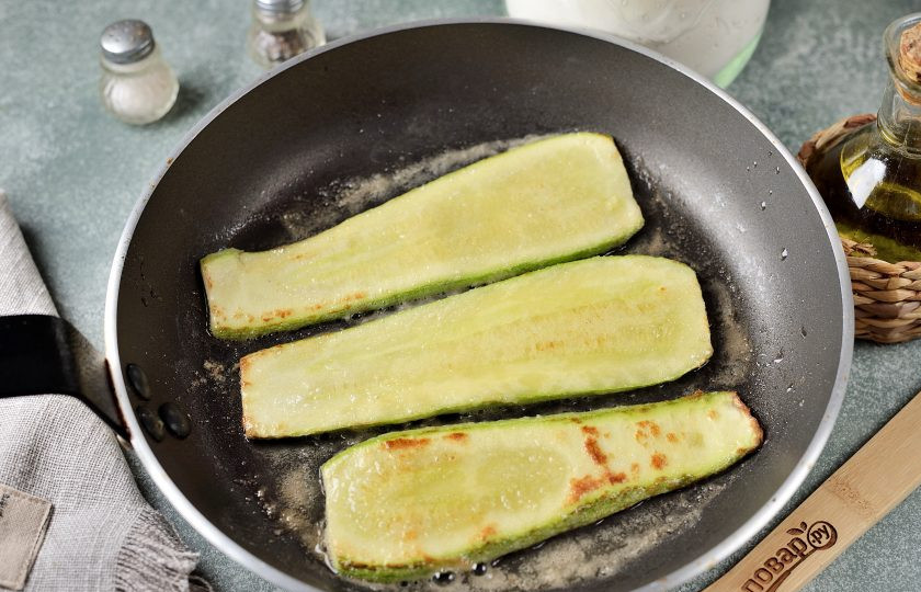 1. Этап. Рулетики из кабачков с огуречно-сырной начинкой: Кабачок нарежьте тонкими ломтиками, слегка запанируйте в муке, обжарьте в разогретом масле по минуте с каждой стороны или до мягкости.