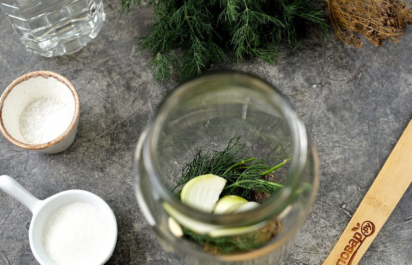 1. Этап. Огурцы маринованные Любимые: Банки и крышки заранее простерилизуйте. На дно банки выложите сухой и свежий укроп, веточку эстрагона, нарезанный зубчик чеснока и пару ломтиков лука, добавьте перцы и лавровый лист.