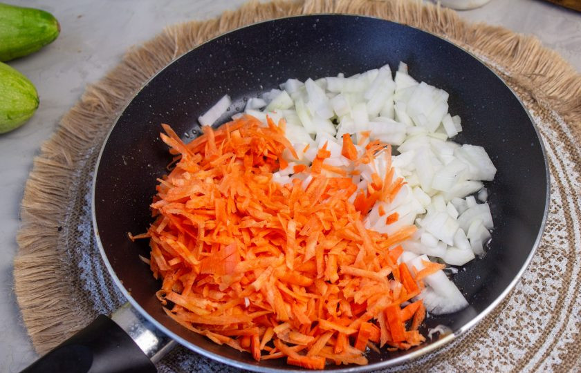 1. Этап. Лазанья из кабачков с грибами: Лук очистите и нарежьте мелким кубиком, морковь — натрите на терке. В сковороду налейте масло, выложите овощи и готовьте при среднем нагреве до их мягкости.