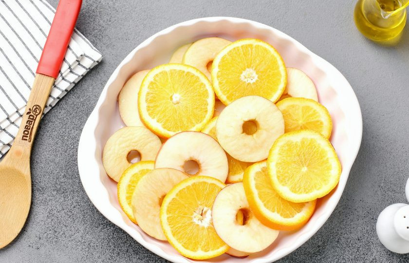 1. Этап. Гусь с яблоками и апельсинами в духовке: Форму для запекания смажьте маслом. Выложите нарезанные кружочками яблоки и апельсин.