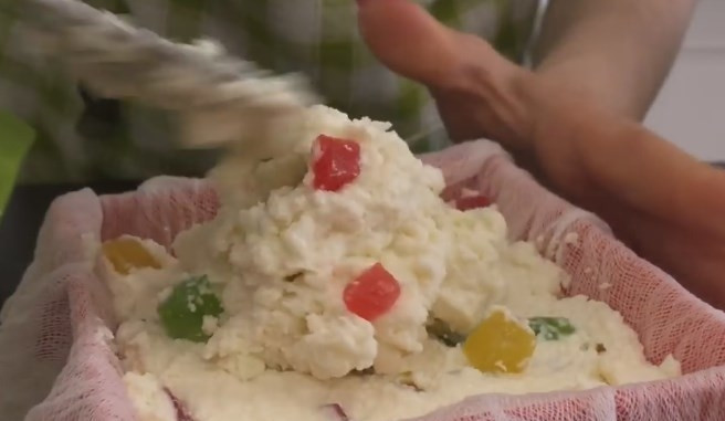 1. Этап. Творожная паска без выпечки с желатином: 5. Разделите творожную массу на части. В одну добавьте цукаты и перемешайте. Форму для кулича застелите влажной марлей, сложенной вдвое, а затем заполните творогом. Сверху накройте марлей, поставьте блюдце и прижмите банкой воды. Отправьте на пару часов в холодильник.