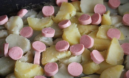 1. Этап. Запеканка с сосиской и картошкой: Картофель лучше всего здесь взять отваренный в мундирах, но подойдет и обычный отварной. Итак, чистим картофель и нарезаем его на ломтики шириной в 0,5-1 см, сосиски также нарезаем на кружочки. Далее смазываем противень небольшим количеством растительного масла и выкладываем на него ровным слоем картофель, на картофель раскладываем кружочки сосиски, солим и перчим все по вкусу.