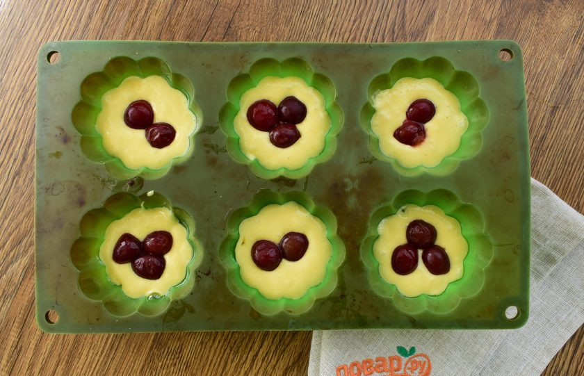 1. Этап. Капкейки с вишней и взбитыми сливками: Выложите тесто в силиконовые формочки для кексов по столовой ложке. В каждую положите по 2-3 вишенки без косточек.
