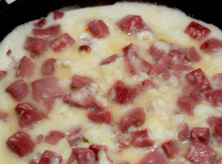 1. Этап. Жареная колбаса: 6. Вливаем взбитые яйца с молоком и накрываем крышкой. Жарим омлет на слабом огне до готовности (примерно 7 минут).