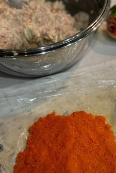 1. Этап. Несладкий мандарин: Рабочую поверхность застилаем пищевой пленкой. Поверх пищевой пленки тонким слоем выкладываем отварную натертую морковь